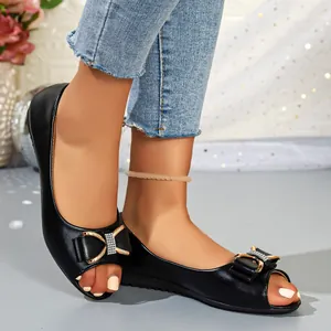 Close-up of black peep-toe flat sandals with diamond-encrusted bow detailing.