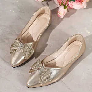 Elegant gold pointed-toe flat with sparkling rhinestone bow detail on a marble surface.