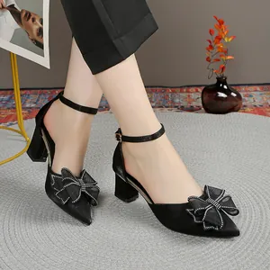 Primer plano de zapatos negros de punta con tacón de bloque, lazo y pedrería.