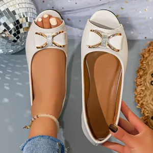 Close-up detail of white flat sandals featuring an elegant bow with crystal accents