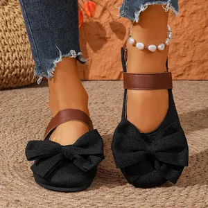 Primer plano de zapatos planos negros con un lazo brillante y correa al tobillo.