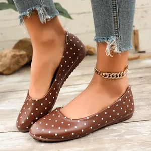 Dettaglio di scarpe basse da donna marroni con pois bianchi su un pavimento in legno rustico