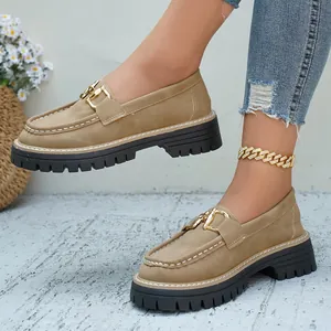Λεπτομέρεια από χακί loafers πλατφόρμας με χρυσή αγκράφα και χοντρές μαύρες σόλες.