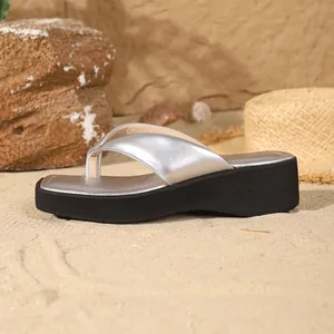 Detail view of silver metallic square-toe platform thong sandals on a beach.
