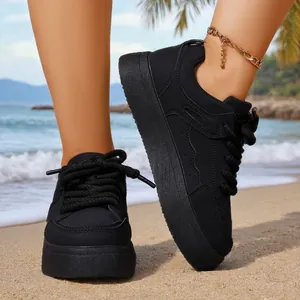 Detailed side view of women's black chunky sneakers with thick laces on the sand.