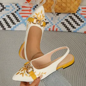 Detailed view of white slingback flat sandals with yellow embroidery and gold chain