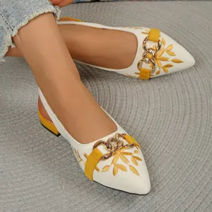 Detail of white pointed-toe slingback flats with yellow embroidery and gold buckle