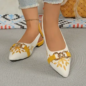 Detailed close-up view of white embroidered slingback sandals with gold chain and pointed toe