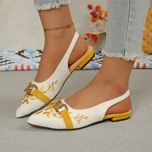 Detailed view of white embroidered slingback flats with gold chain and yellow accents.