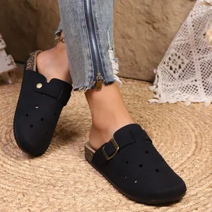 Close-up of stylish black closed-toe mules worn with jeans on a rustic straw mat background.