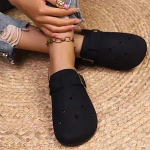 Black closed-toe suede clogs with buckle strap and breathable holes on a woven mat