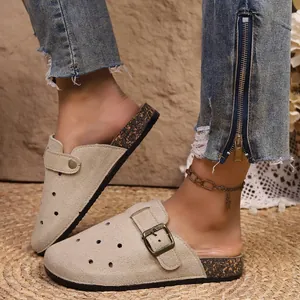 Detail view of beige suede perforated clogs with cork-textured sole and buckle strap.
