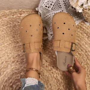 Close-up of tan buckled clogs with perforated design on a straw mat background.