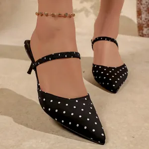 Detalle de mules de lunares negros con punta fina y tacones de aguja elegantes.