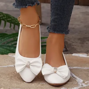 Close-up of white pointed-toe flats with decorative rhinestone bowknot for women.