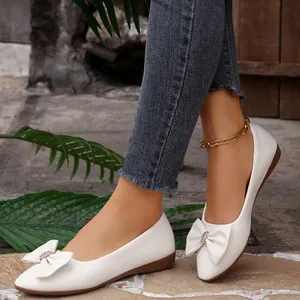 Detail view of elegant white pointed-toe flats with a stylish bow embellishment.