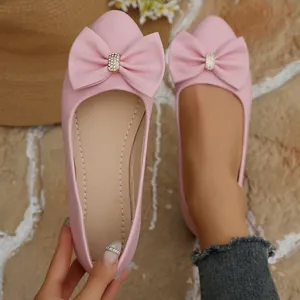 Close-up of pink pointed toe flats featuring a large bow and sparkling rhinestones