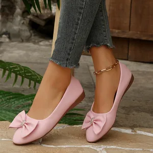 Close-up of pink pointed-toe ballet flats with rhinestone bow and gold anklet detail.