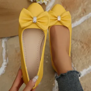 Detailed view of yellow pointed-toe flat shoes featuring a stylish rhinestone-accented bowknot
