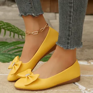 Detail shot of elegant yellow pointed-toe ballet flats featuring a rhinestone bow