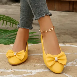 Close-up detail of stylish yellow pointed-toe flat shoes featuring a rhinestone bowknot.