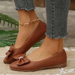 Detailed macro view of stylish brown bow-knot pointed-toe flat shoes worn with denim jeans