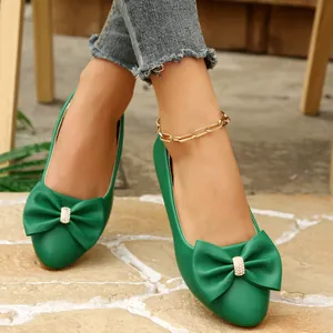 Close-up detail of stylish green flat slip-on shoes with an elegant bow and rhinestones