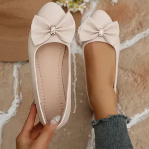 Detail showing beige pointed-toe flat shoes with a large rhinestone-decorated bow.