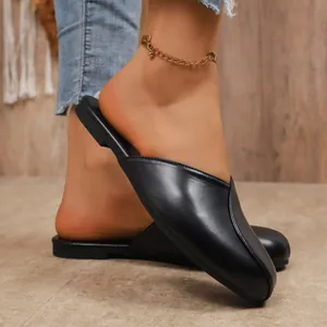 Close-up of black pointed-toe flat mules on a model in a cozy indoor setting.