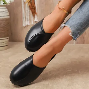 Detailed view of women's black round-toe flat mules worn on feet in a cozy indoor setting