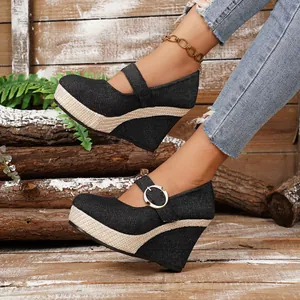Close-up detail of black denim wedge platform shoes with buckle strap and woven trim