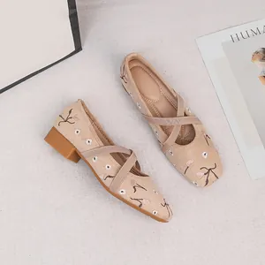 Nahaufnahme von beigen Mary Jane Flats mit zarter Blumenstickerei und Kreuzbändern