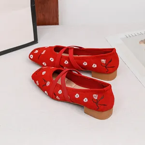Detailaufnahme roter Wildleder-Mary-Janes mit Blumenstickerei und Kreuzriemen.