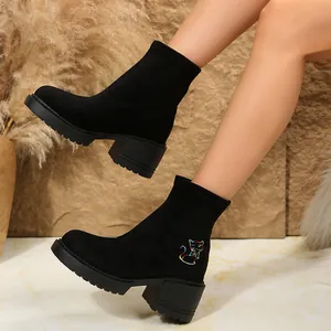 Close-up view of black suede ankle boots with colorful cat embroidery on chunky heels