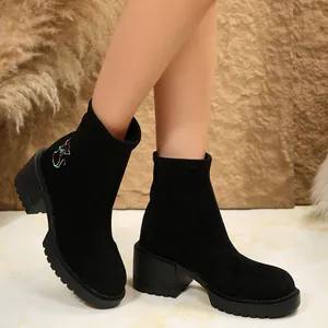 Close-up of black suede ankle boots with colorful cat embroidery and a sturdy block heel.