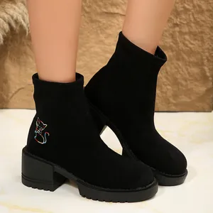 Close-up of black suede ankle boots featuring colorful cat embroidery and block heel.