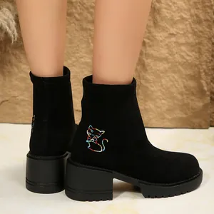 Close-up of black suede ankle boots featuring colorful kitten embroidery and square heel
