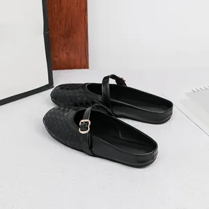 Close-up detail of black woven round-toe flat mules with gold buckle strap decoration