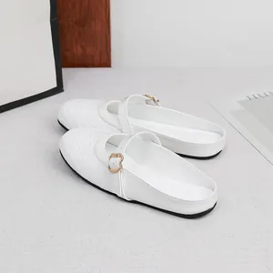 Detailed view of white woven flat mules with buckle strap on a neutral background.