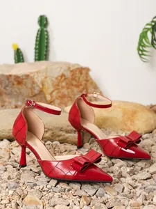 Close-up of red stiletto pumps featuring a triple-layered bow and elegant ankle strap.