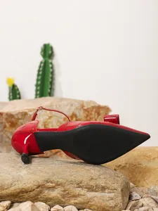 Detailed bottom view of elegant red pointed toe high heels with bow and slingback strap