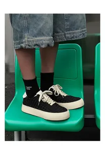 Close-up of black hand-woven low-top sneakers worn by a model on a green chair