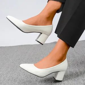 A detailed view of elegant white patent leather block heel pumps worn by a model