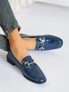 Detalle de mocasines azules con efecto cocodrilo y hebilla de bocado con pedrería.