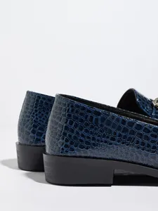 Primer plano de la textura de cocodrilo azul y el tacón negro de los mocasines de mujer.