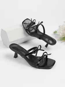 Detailansicht eleganter schwarzer Sandalen mit Pfennigabsatz, Schleifenakzenten und Karree-Zehe.