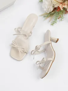 Elegante beige Sandaletten mit Pfennigabsatz, doppelten Schleifen und modischer Karree-Form.