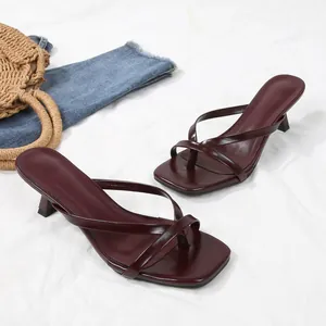 Detailed shot of burgundy square-toe thong sandals with kitten heels on a white fabric.