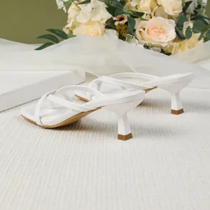 Detail shot of white square toe kitten heel thong sandals with elegant floral backdrop