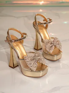Close-up of golden platform sandals featuring a sparkling rhinestone bow and mesh